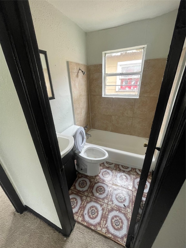 full bath with a textured wall, toilet, bathing tub / shower combination, and vanity
