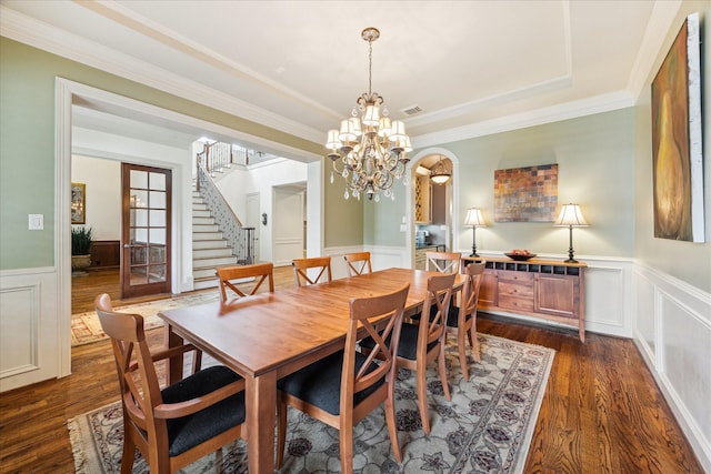 dining space with stairway, a chandelier, a wainscoted wall, dark wood finished floors, and crown molding