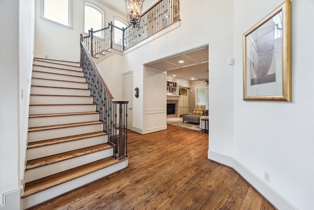 stairway featuring wood finished floors, a brick fireplace, a towering ceiling, a chandelier, and baseboards
