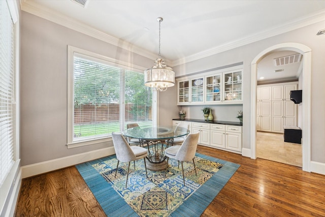 dining area with arched walkways, wood finished floors, baseboards, ornamental molding, and a chandelier