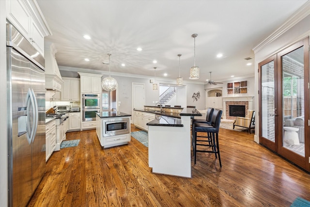 kitchen featuring built in appliances, dark countertops, a spacious island, a brick fireplace, and dark wood finished floors