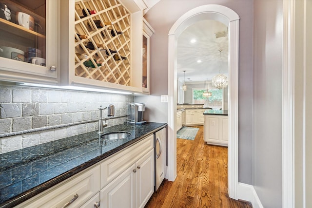 indoor wet bar with light wood-style flooring, decorative backsplash, arched walkways, pendant lighting, and recessed lighting