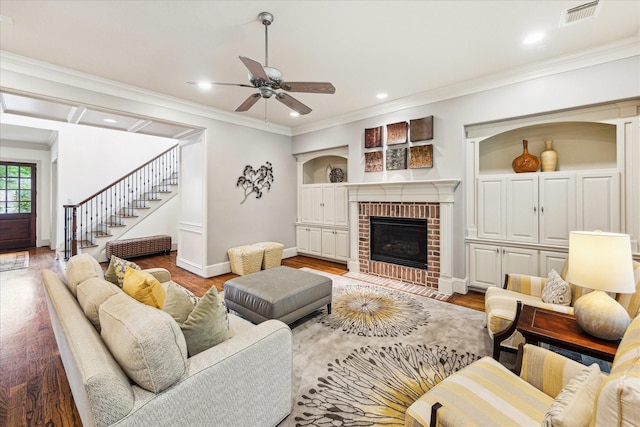 living area featuring ceiling fan, wood finished floors, crown molding, baseboards, and a brick fireplace