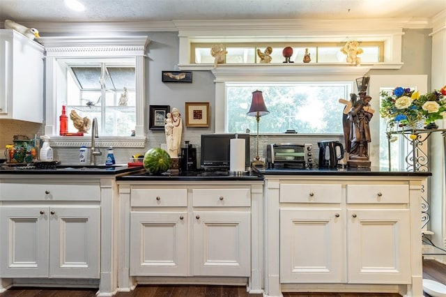 kitchen featuring dark countertops, tasteful backsplash, white cabinets, crown molding, and a sink