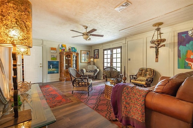living room featuring ceiling fan, a textured ceiling, wood finished floors, a decorative wall, and attic access