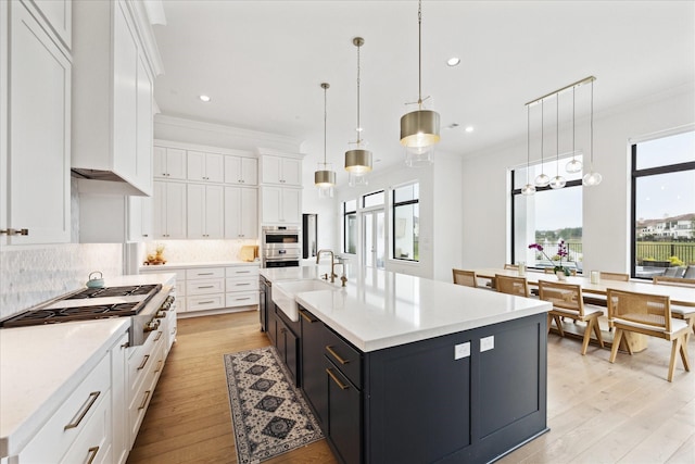 kitchen with a sink, stainless steel gas cooktop, light countertops, white cabinets, and ornamental molding