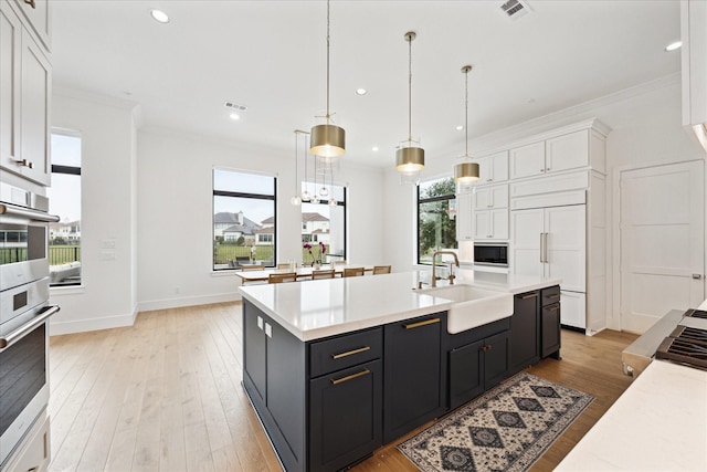 kitchen featuring a sink, built in appliances, white cabinetry, light countertops, and crown molding