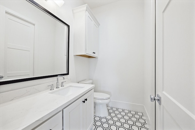 half bath with toilet, vanity, baseboards, and tile patterned floors