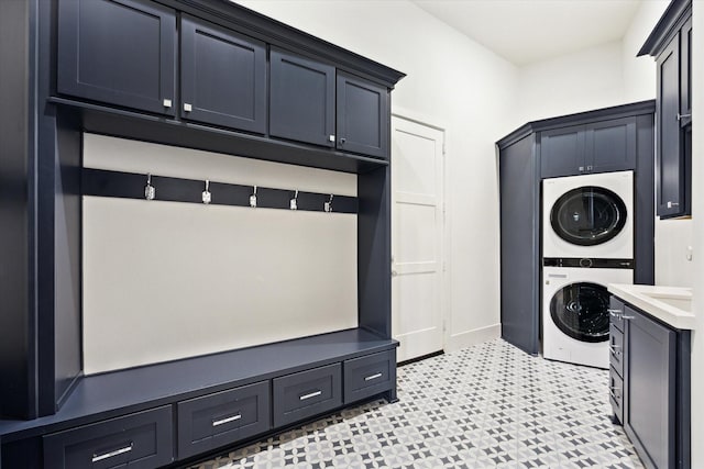 laundry area featuring stacked washer and clothes dryer, cabinet space, light floors, and baseboards