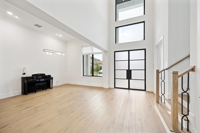 foyer entrance featuring light wood-style flooring, a towering ceiling, baseboards, stairway, and ornamental molding