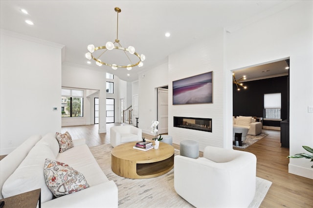 living room featuring a chandelier, light wood-style flooring, recessed lighting, a fireplace, and crown molding