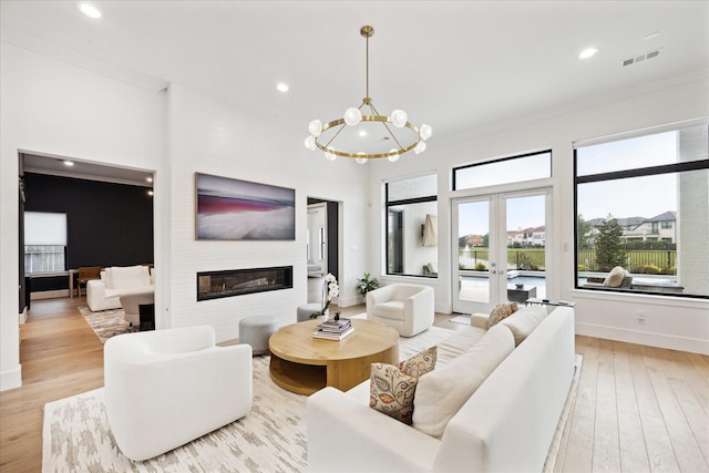 living area featuring light wood finished floors, a glass covered fireplace, baseboards, a chandelier, and recessed lighting