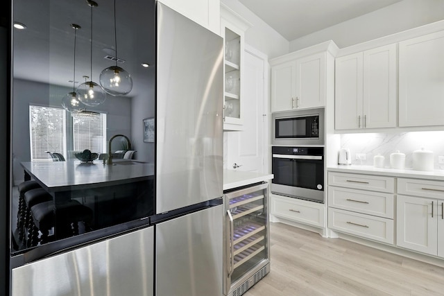 kitchen featuring appliances with stainless steel finishes, beverage cooler, a sink, white cabinets, and light wood-style floors