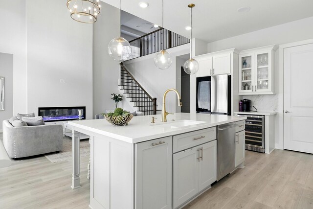 kitchen featuring a sink, stainless steel appliances, wine cooler, a glass covered fireplace, and light wood-style flooring