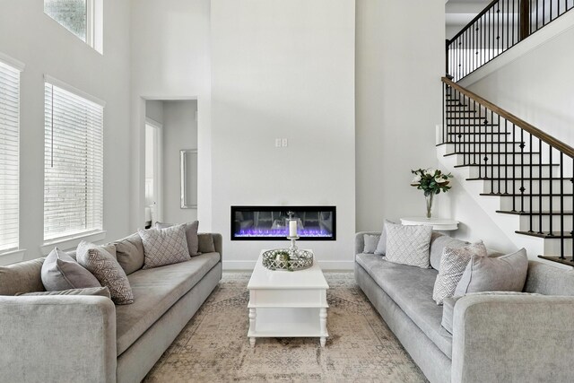 living room with a towering ceiling, a glass covered fireplace, stairway, and baseboards