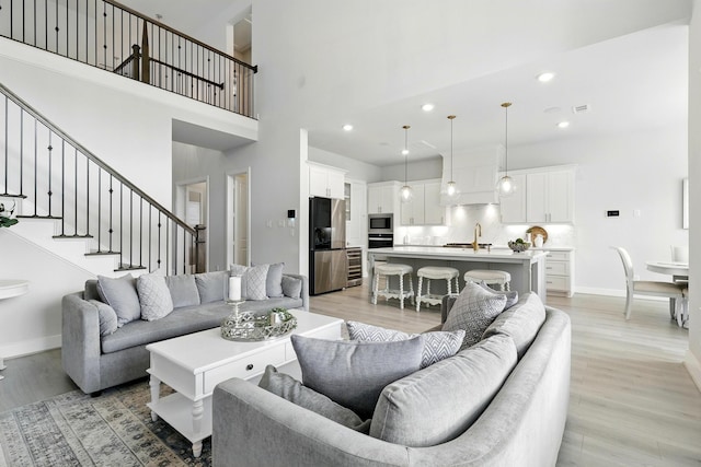 living room with light wood-type flooring, baseboards, a towering ceiling, recessed lighting, and stairway