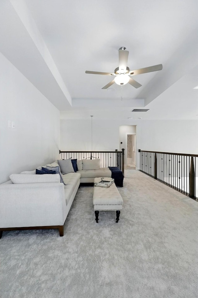 carpeted living room featuring a ceiling fan and a raised ceiling