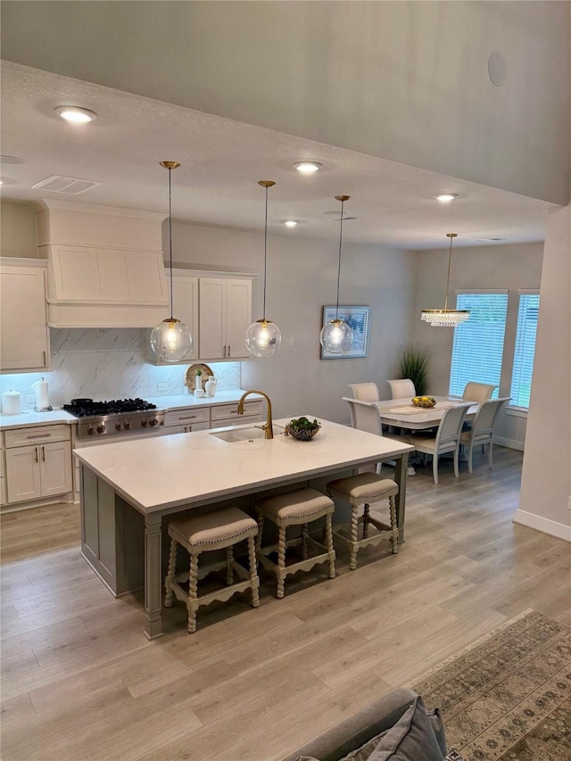 kitchen featuring a sink, stainless steel gas stovetop, tasteful backsplash, white cabinets, and light countertops