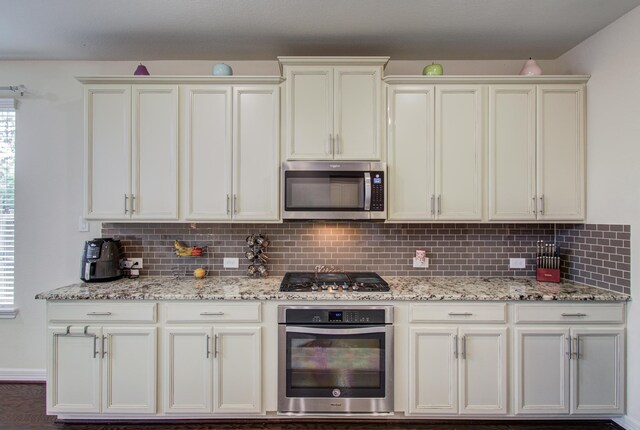 kitchen featuring appliances with stainless steel finishes, backsplash, and light stone countertops