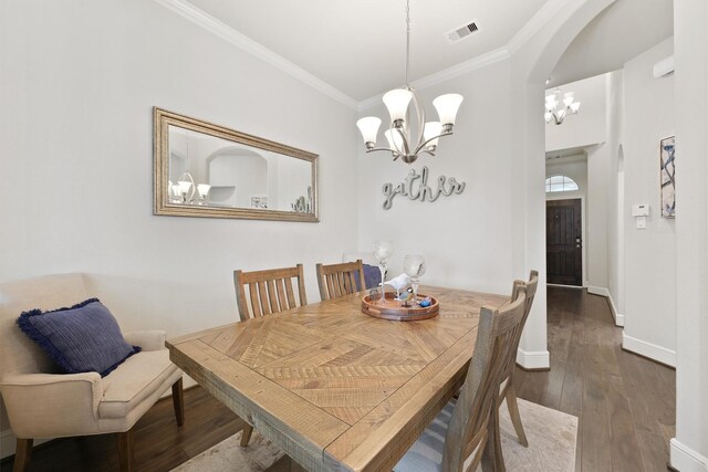 dining space with a chandelier, crown molding, hardwood / wood-style flooring, arched walkways, and baseboards