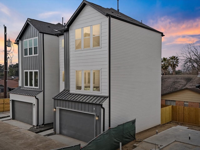 249 De Boll Ave, Houston, TX 77022 - property exterior at dusk with board and batten siding, a standing seam roof, fence, a garage, and metal roof