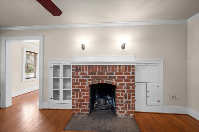 detailed view of wood finished floors, ornamental molding, baseboards, a brick fireplace, and a ceiling fan