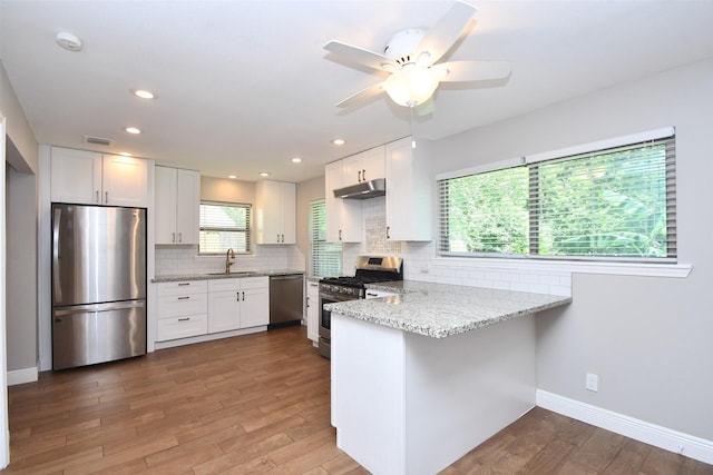 kitchen featuring appliances with stainless steel finishes, a peninsula, white cabinets, under cabinet range hood, and light stone countertops