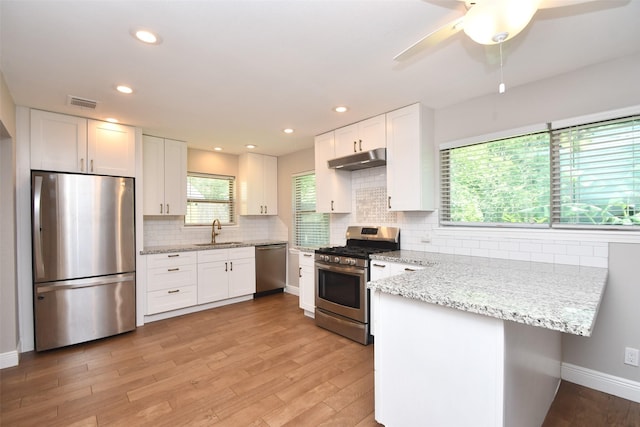 kitchen featuring appliances with stainless steel finishes, under cabinet range hood, a peninsula, a sink, and white cabinetry