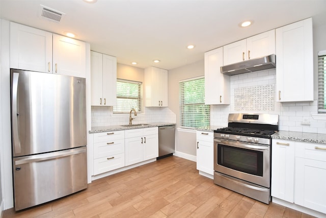 kitchen featuring stainless steel appliances, under cabinet range hood, a sink, white cabinets, and light wood-type flooring