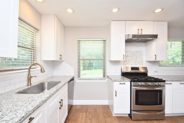 kitchen with appliances with stainless steel finishes, under cabinet range hood, a sink, baseboards, and white cabinets