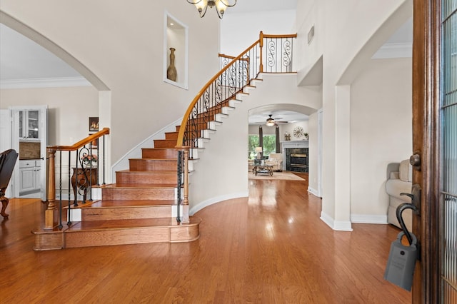 foyer featuring stairs, a glass covered fireplace, a ceiling fan, wood finished floors, and arched walkways