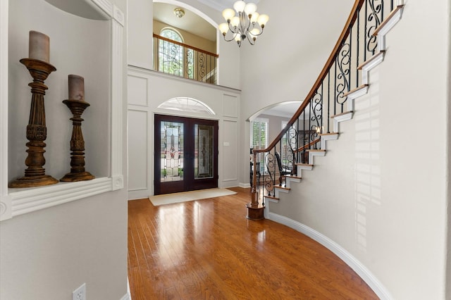 entrance foyer with arched walkways, a chandelier, wood finished floors, stairway, and a towering ceiling