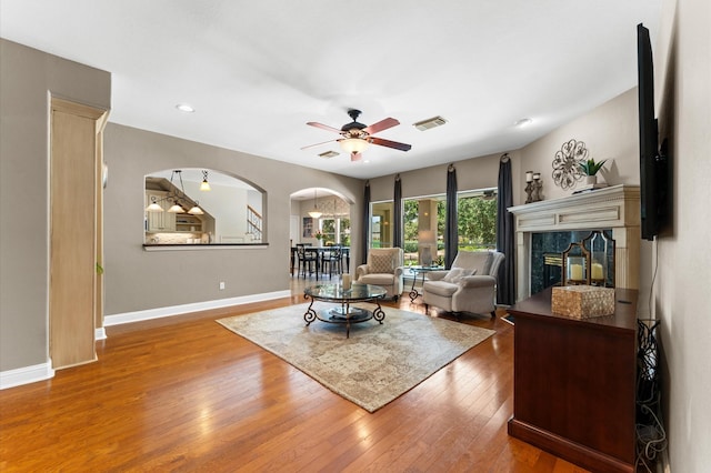 living room featuring arched walkways, wood-type flooring, baseboards, ceiling fan, and a fireplace