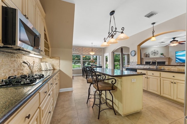 kitchen featuring stainless steel microwave, a sink, tasteful backsplash, gas stovetop, and arched walkways