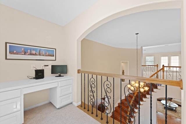 hallway with an office area, light colored carpet, baseboards, and arched walkways