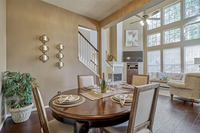 70 Harvest Wind Pl, The Woodlands, TX 77382 - dining area featuring a ceiling fan, dark wood-type flooring, a glass covered fireplace, baseboards, and a towering ceiling