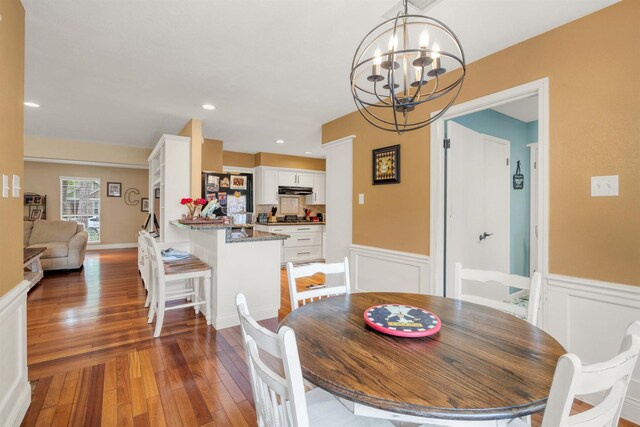 dining room with hardwood / wood-style flooring, a chandelier, a wainscoted wall, and a decorative wall