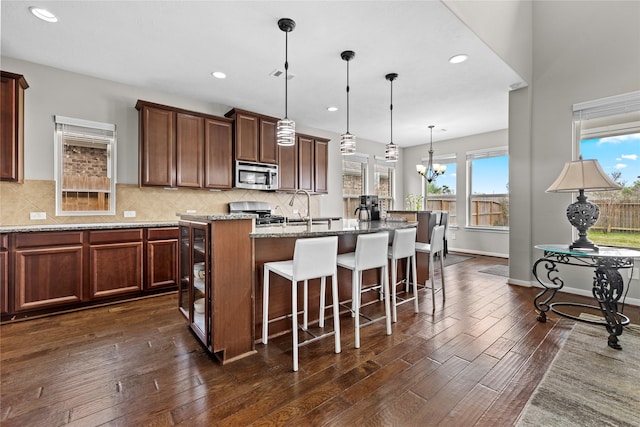 22726 Little Blue Stem Dr, Tomball, TX 77375 - kitchen featuring stainless steel microwave, a kitchen island with sink, dark wood-style floors, a kitchen bar, and light stone counters