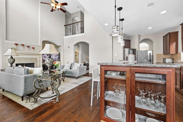 22726 Little Blue Stem Dr, Tomball, TX 77375 - interior space featuring a ceiling fan, a tiled fireplace, visible vents, dark wood-style flooring, and arched walkways