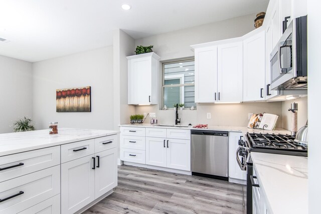 kitchen with appliances with stainless steel finishes, a sink, white cabinets, light wood-style floors, and recessed lighting