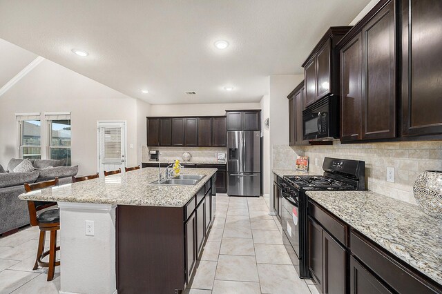 kitchen with black appliances, a sink, open floor plan, tasteful backsplash, and a kitchen breakfast bar