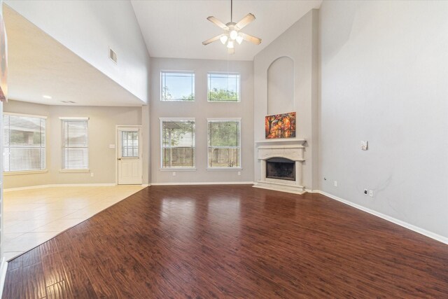 unfurnished living room featuring a fireplace with raised hearth, ceiling fan, high vaulted ceiling, baseboards, and wood finished floors