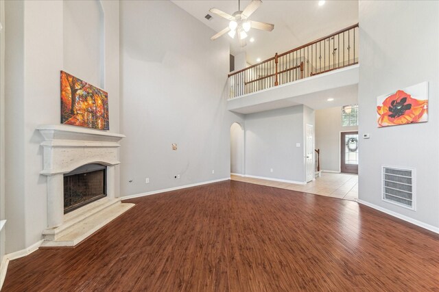 unfurnished living room with high vaulted ceiling, a fireplace with raised hearth, wood finished floors, a ceiling fan, and baseboards