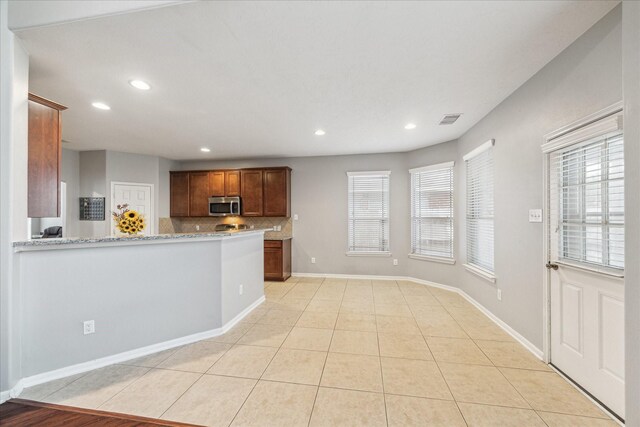 kitchen with stainless steel microwave, recessed lighting, light stone counters, decorative backsplash, and baseboards