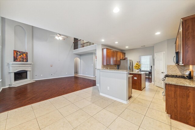 kitchen featuring stainless steel appliances, light tile patterned floors, ceiling fan, a fireplace with raised hearth, and decorative backsplash