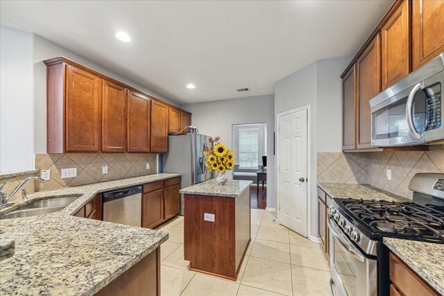 kitchen with appliances with stainless steel finishes, a sink, light stone counters, a kitchen island, and recessed lighting