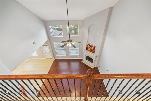 staircase with ceiling fan, a fireplace with flush hearth, wood finished floors, baseboards, and a high ceiling