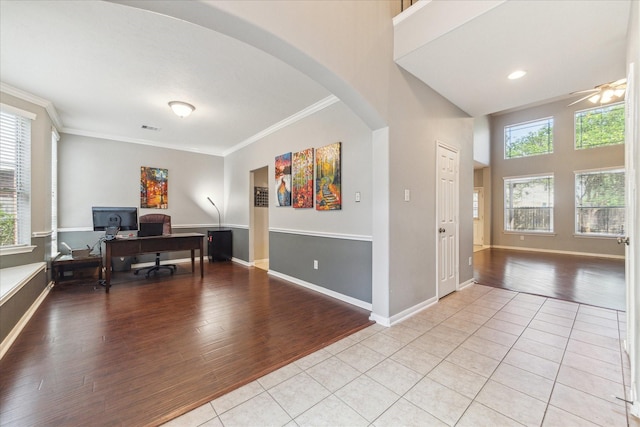 home office featuring arched walkways, light wood-style flooring, ornamental molding, a ceiling fan, and baseboards