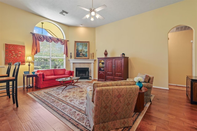 living area with a ceiling fan, wood-type flooring, a fireplace, arched walkways, and baseboards