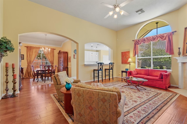 living area featuring ceiling fan, wood-type flooring, a chandelier, arched walkways, and a towering ceiling